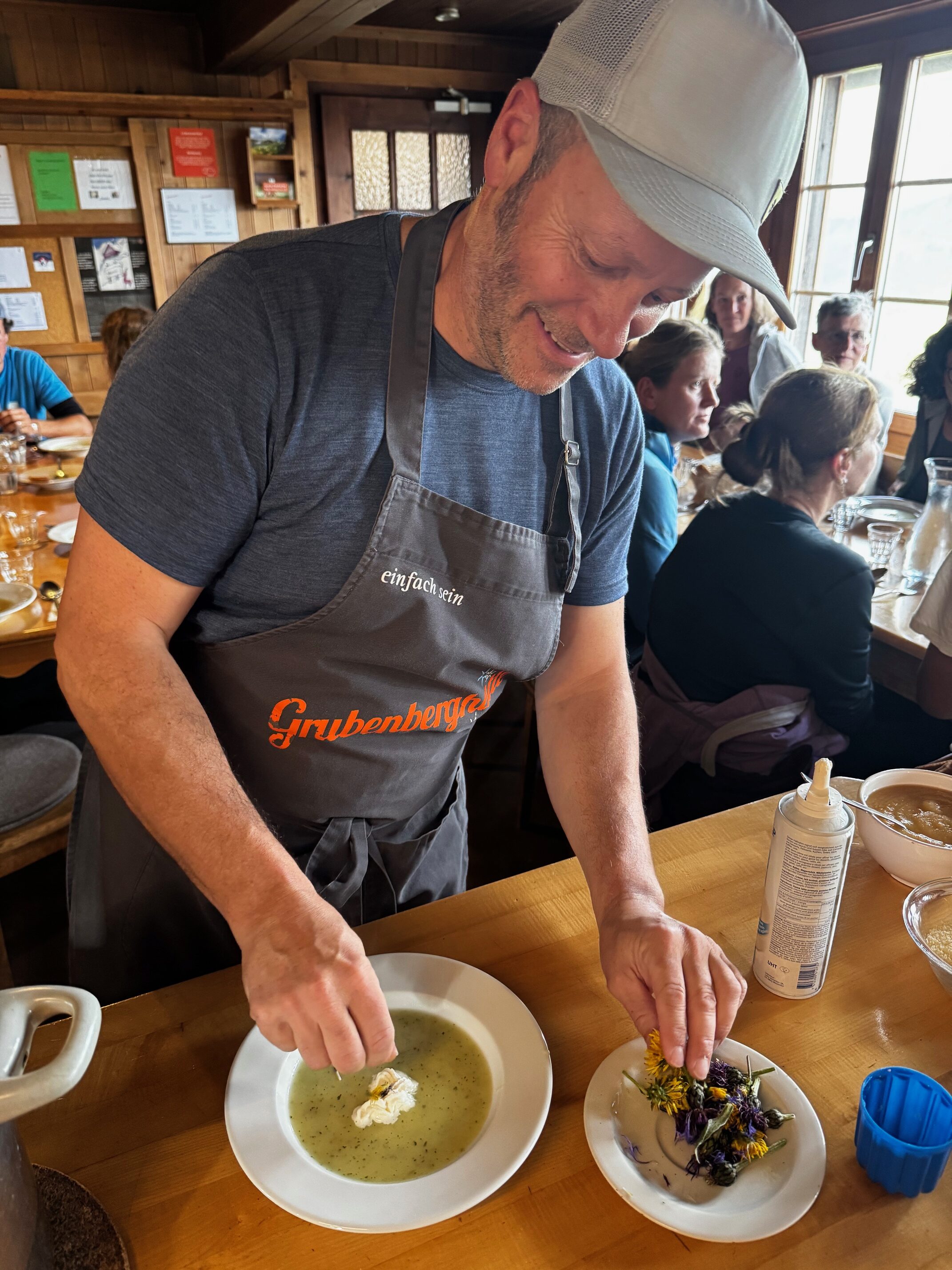 Mann dekoriert Suppe mit Sahne und Blumen in einem rustikalen Restaurant. Lächelnd und konzentriert am Tisch.